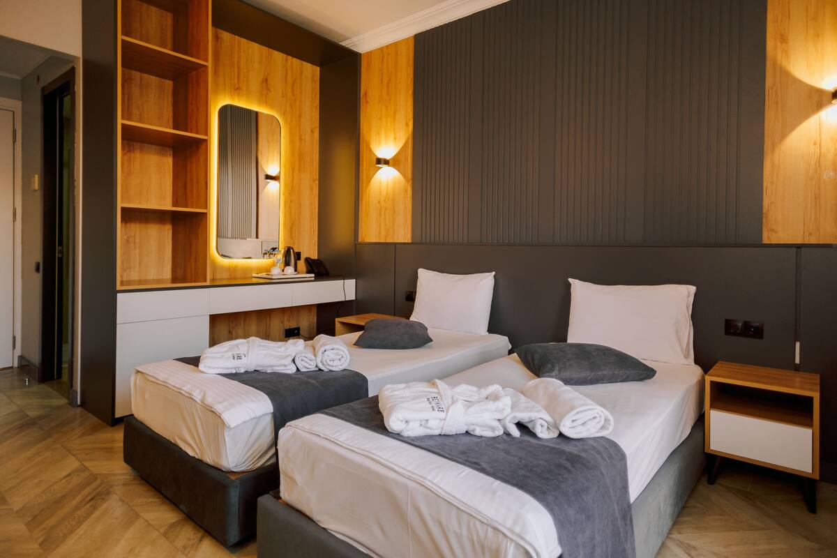 A modern hotel room with two beds, a large mirror, and built-in wooden shelving.