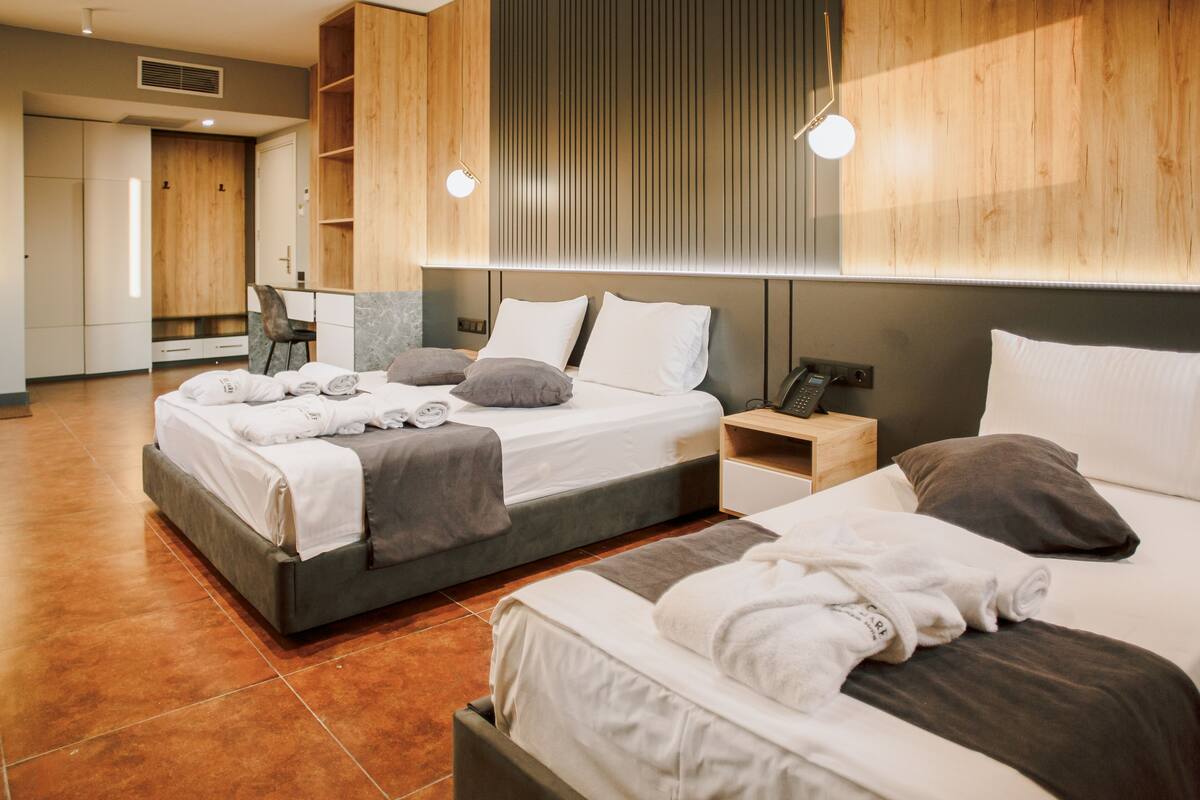 A modern hotel room with two beds, a wooden wardrobe, a desk, and a chair.