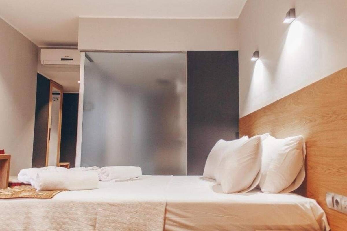 A hotel room with a bed, pillows, a bedside table, and a wall-mounted light fixture.