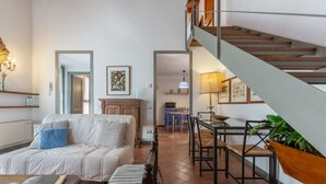 Un saló amb sofà, taula de centre, escala i zona de menjador amb cadires i taula.