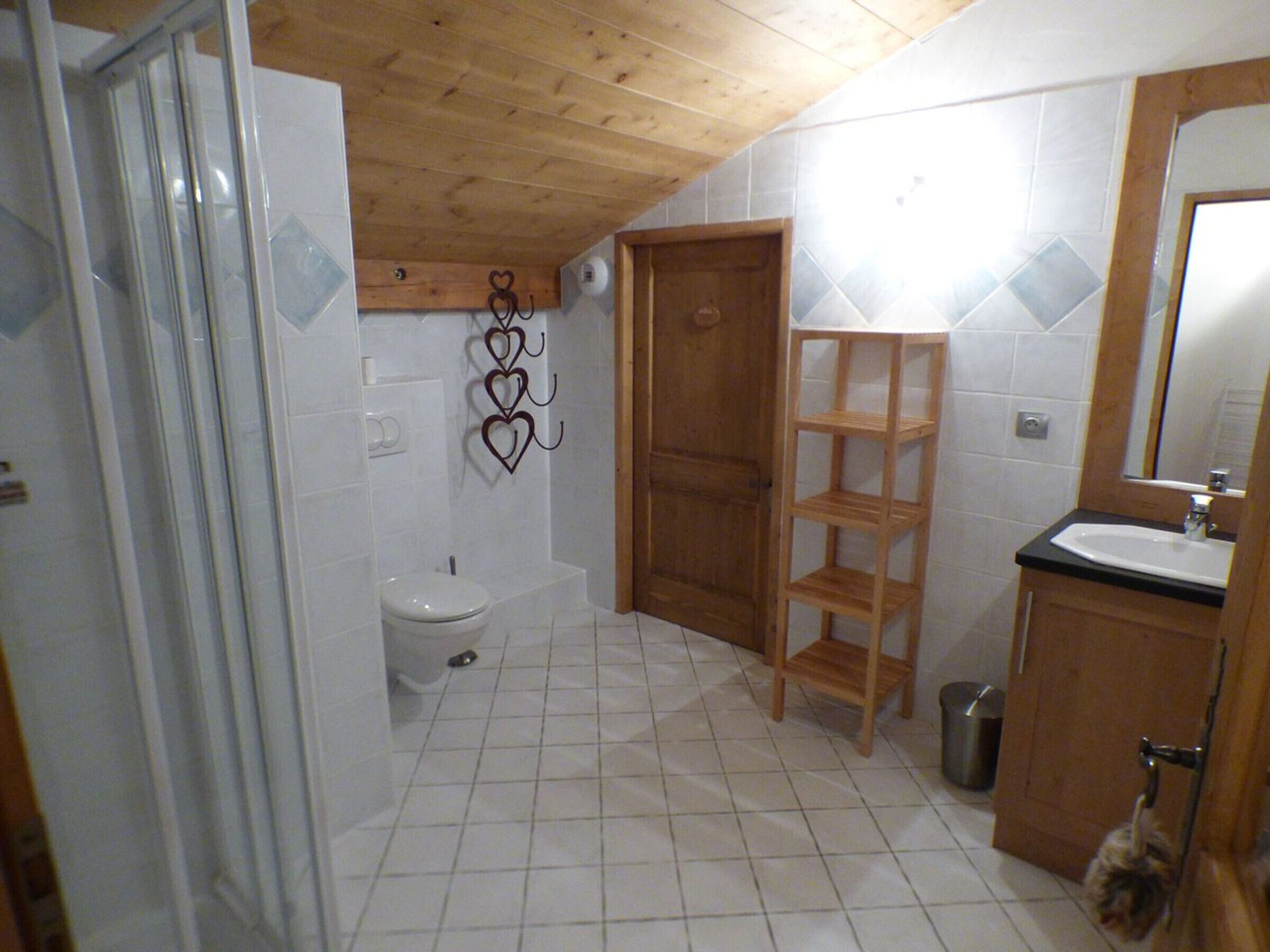 Een kleine badkamer met betegelde wanden, een houten deur, een toilet, een wastafel en een spiegel.