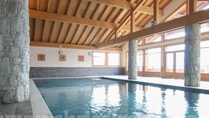 Una piscina interior con pilares de piedra, vigas de madera y grandes ventanales.