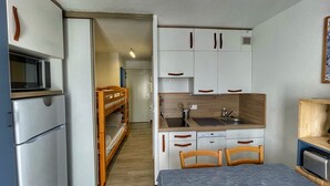 A compact kitchen with white cabinets, a microwave, and a sink. There is a dining area with a table and chairs. - Cozy Studio for 5, Near Ski Lift and Shops, South-Facing Balcony, Flaine Forest - Doris Residence (Flaine)