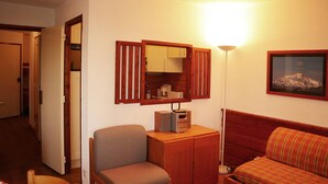 Une pièce de taille modeste, comprenant un bureau en bois, une chaise, un canapé, une petite table et une lampe.