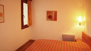 Une chambre d’hôtel avec un lit, une table de chevet, une lampe, une fenêtre avec des rideaux et un tableau encadré au mur.