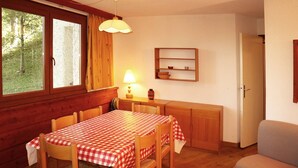 Une pièce confortable, aménagée comme un chalet, avec une table à manger en bois, des chaises, une lampe et une petite étagère sur laquelle se trouvent un panier et un verre.