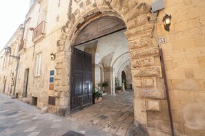 A stone building with a large arched doorway, potted plants, and a number plaque. - Basseo33 Suite (Lecce)
