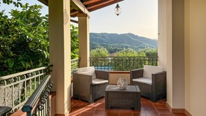 Ein Balkon mit Korbmöbeln, Blick auf eine grüne Landschaft und einen klaren Himmel.