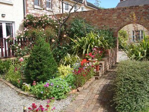 Ein Garten mit verschiedenen Pflanzen und Blumen, einer Ziegelmauer und einem Weg.