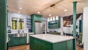 A kitchen with green cabinets, a white island, stainless steel appliances, and pendant lighting.