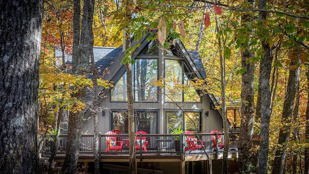 A cabin with a balcony, surrounded by trees with autumn foliage.