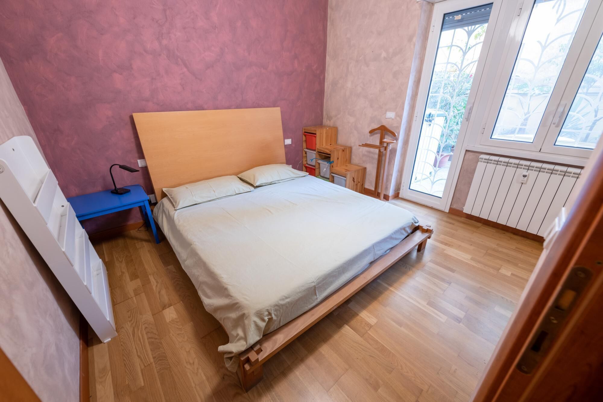Une chambre à coucher avec un lit en bois, un bureau, une chaise, un radiateur et une fenêtre donnant sur un paysage verdoyant.