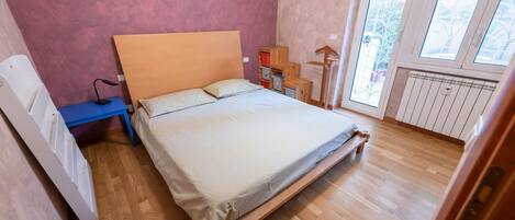 Une chambre à coucher avec un lit en bois, un bureau, une chaise, un radiateur et une fenêtre donnant sur un paysage verdoyant.