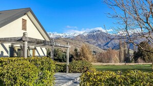 A house with a covered porch, a mountain backdrop, and well-maintained hedges.