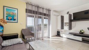 A modern living room with a sofa, a coffee table, a chair, a TV, and a large window with sheer curtains. - Cozy apartment in Barbat na Rabu (Barbat na Rabu)