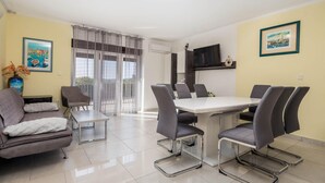 A dining area with a table and chairs, a sofa, a TV, and a window with curtains. - Cozy apartment in Barbat na Rabu (Barbat na Rabu)