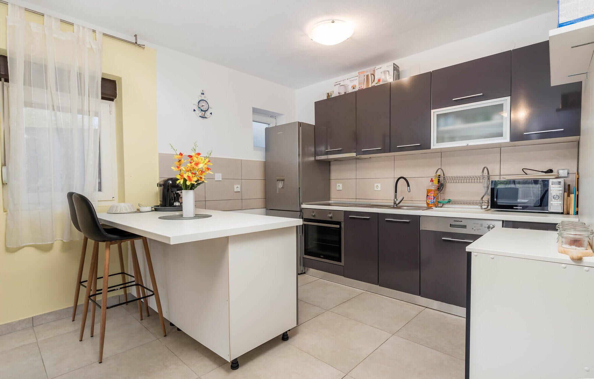 A modern kitchen with a central island, dark cabinets, a microwave, and a coffee maker.