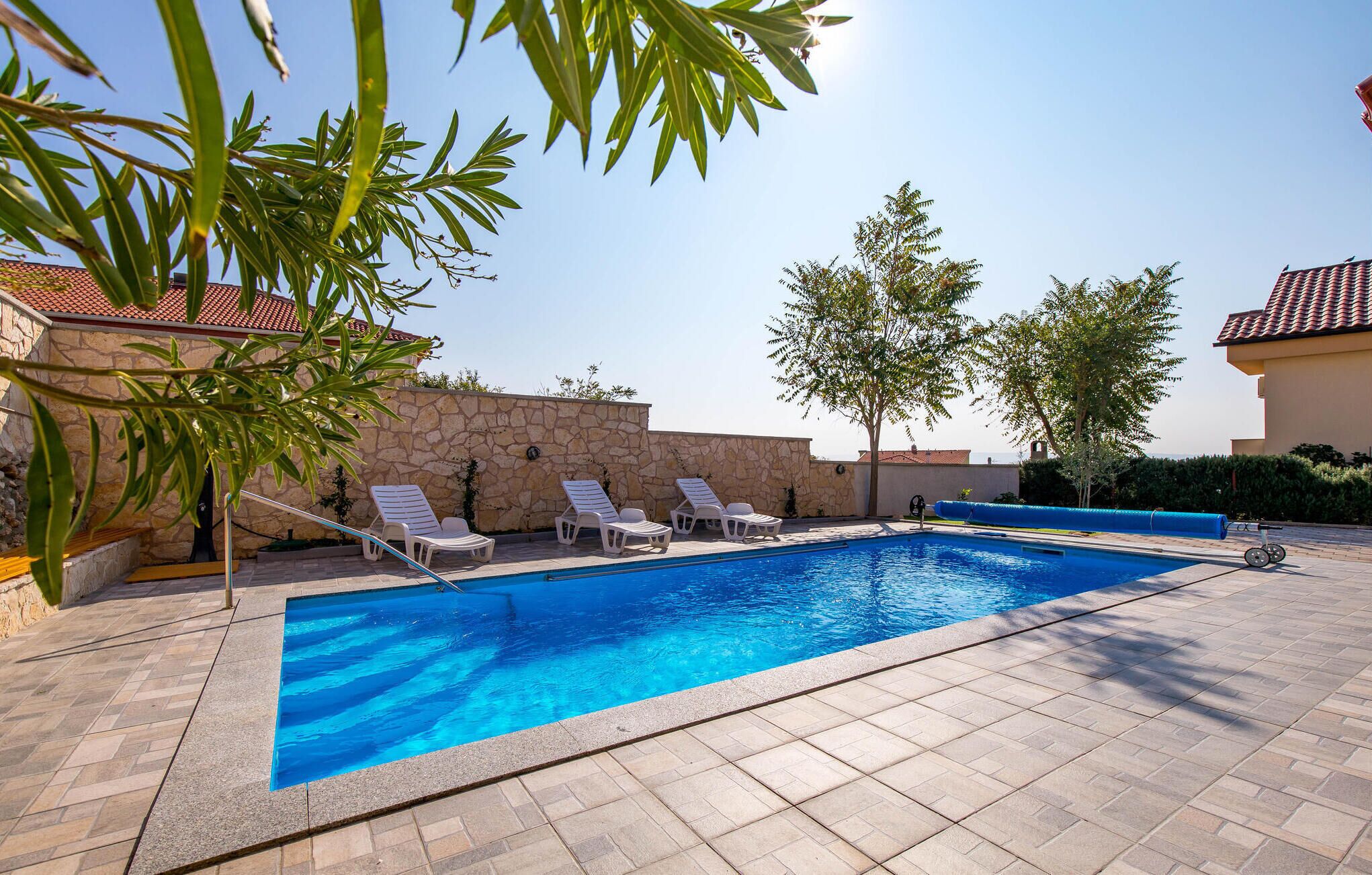 A swimming pool with lounge chairs, a stone wall, and a clear blue sky.