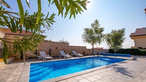 A swimming pool with lounge chairs, a stone wall, and a clear blue sky. - Cozy apartment in Barbat na Rabu (Barbat na Rabu)