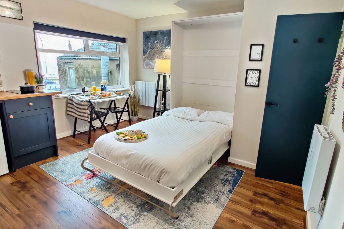 Un dormitorio pequeño con cama, mesita de noche y un rincón de escritorio con silla.