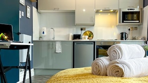 Una habitación de hotel moderna con cama, escritorio, televisor, zona de cocina y baño.