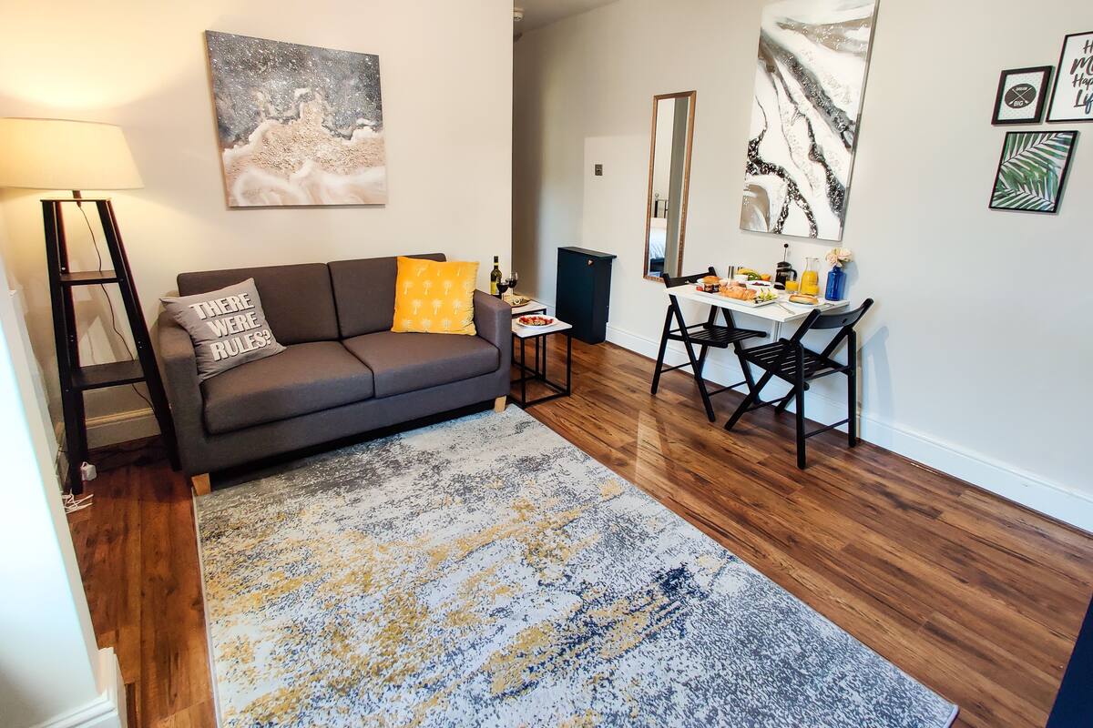 Una sala moderna con un sofá gris, una mesa de centro y un comedor con una mesita y sillas.