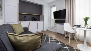 Een moderne woonruimte met een grijze bank, een witte eettafel en een keuken met grijze kastjes en een flatscreen televisie.