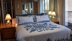 A neatly made bed with a floral bedspread, two bedside lamps, a nightstand, a mirror, and a window with curtains.