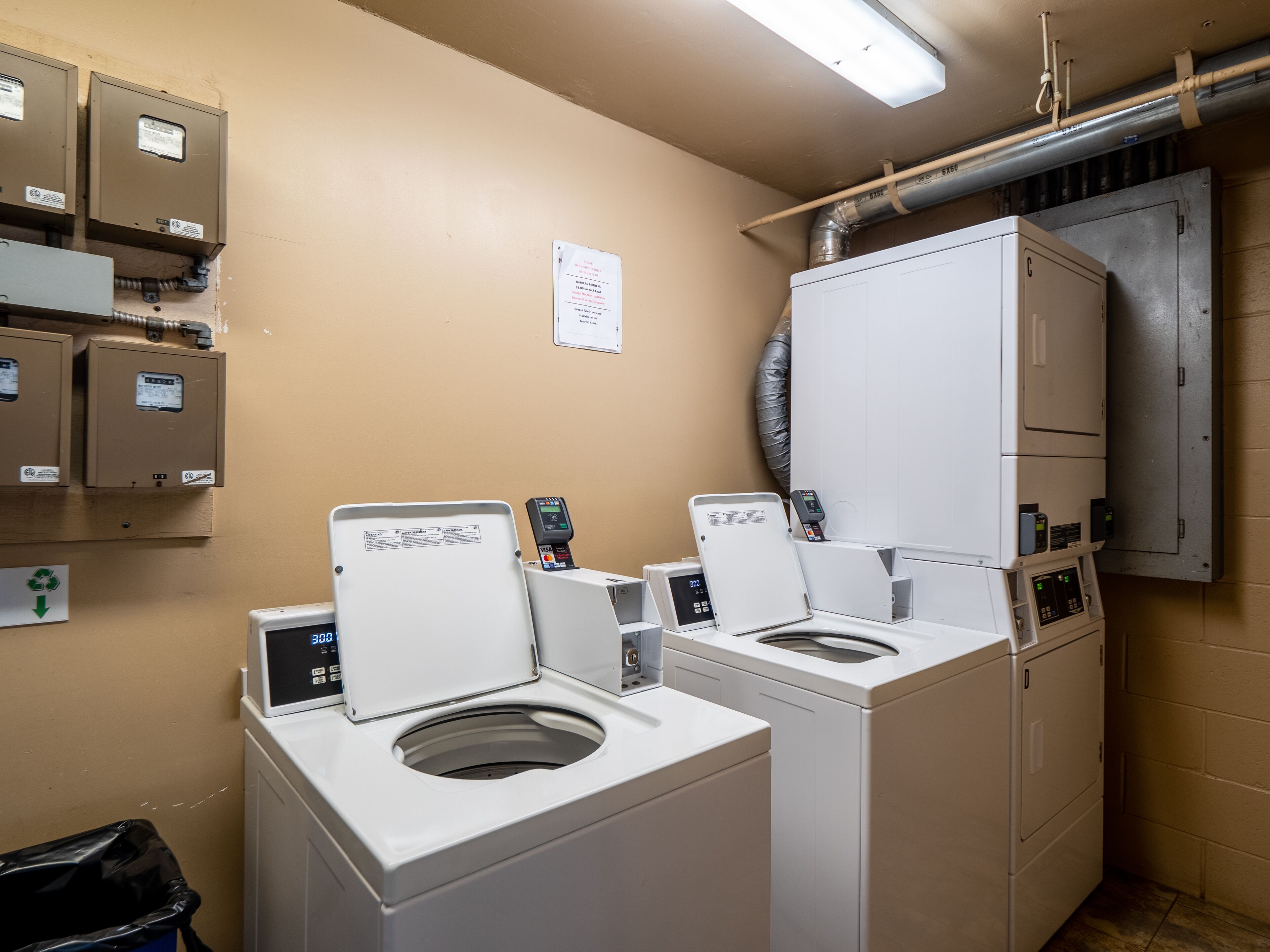 A laundry room with two front-loading washing machines, a dryer, and a utility room with electrical panels.