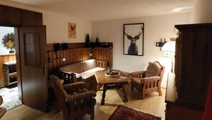 Tunnelmallinen olohuone, jossa on puinen sohva, nojatuoleja, sohvapöytä ja kuviollinen matto.