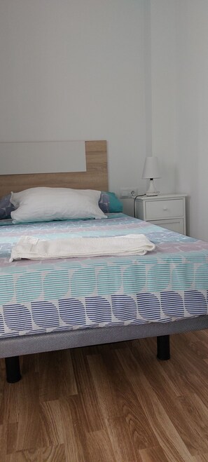 A neatly made bed with a patterned bedspread, a wooden headboard, a bedside lamp, and a nightstand with a drawer.