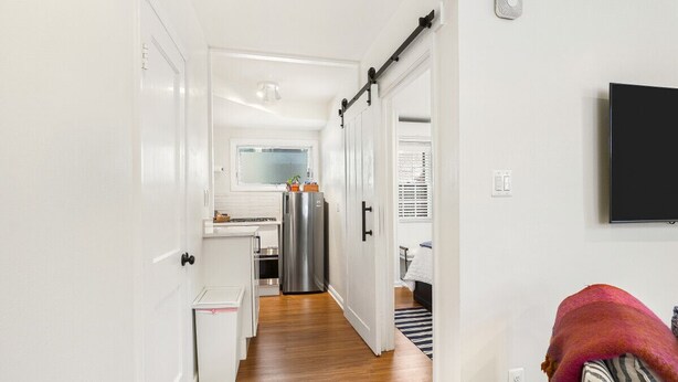 A narrow hallway leading to a kitchen with a refrigerator, a small countertop, and a window.