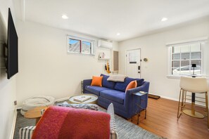 A living room with a sofa, a small round table, a chair, a television, and a window.