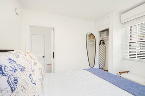 A bedroom with a bed, a wardrobe, a mirror, and a window with blinds.