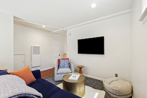 Un salon moderne comprenant un canapé, un fauteuil, une table basse ronde et un téléviseur à écran plat fixé au mur.