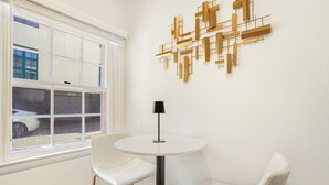 A room with a white round table, two white chairs, a black floor lamp, and a geometric wall art piece.