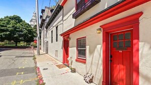 A street view with a building featuring red doors and windows, a white facade, and a stop sign in the background.