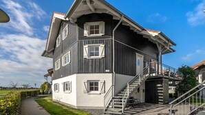 A two-story building with a staircase leading to a balcony, surrounded by a well-maintained lawn and a clear sky. - Nice apartment in Bogense with WiFi (Bogense)