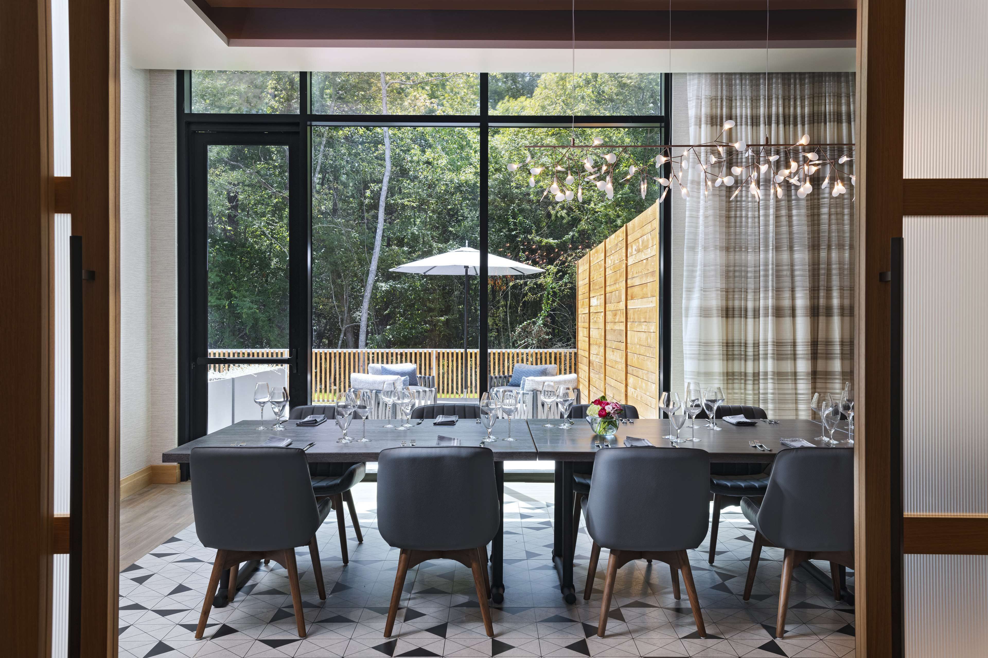 Un coin repas avec une grande fenêtre, une table dressée pour six personnes et une vue sur une terrasse en bois et des arbres.