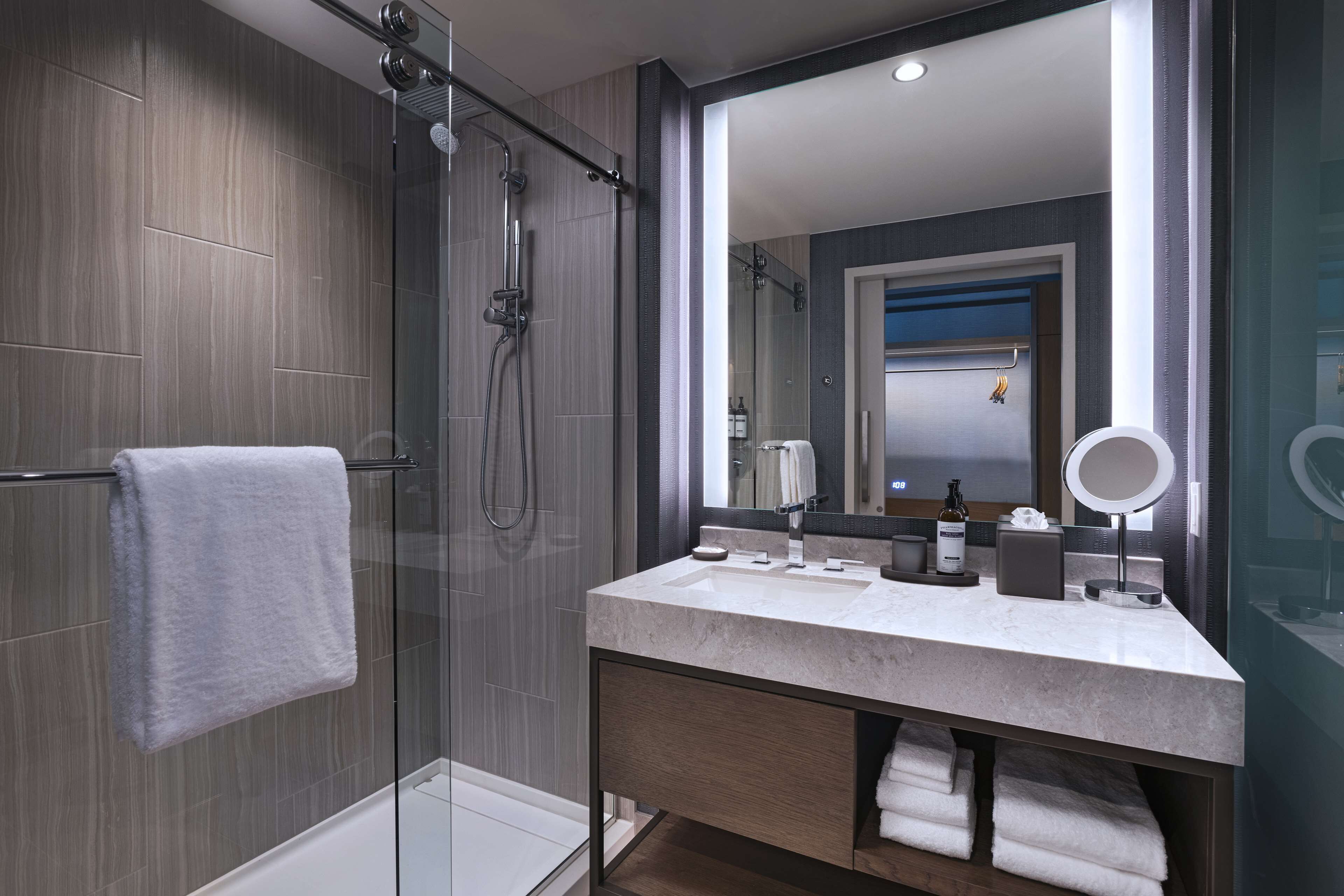 Un baño moderno con cabina de ducha acristalada, un espejo grande y un tocador con encimera de mármol.