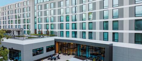 A modern hotel with a flat roof, large windows, and an outdoor patio area with seating and greenery.