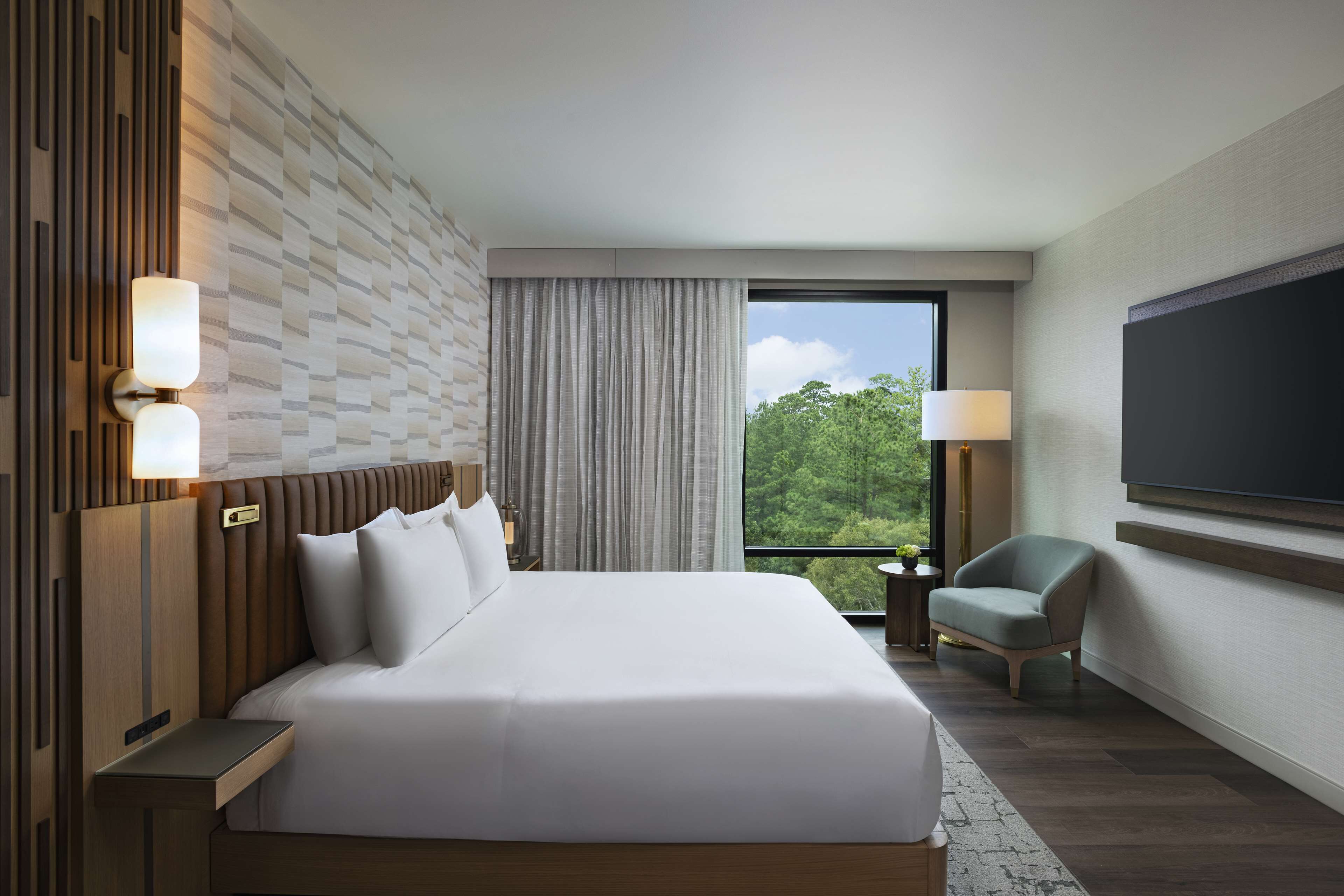 Une chambre d’hôtel moderne dotée d’un grand lit, d’une télévision à écran plat, d’un coin salon et offrant une vue sur l’extérieur.