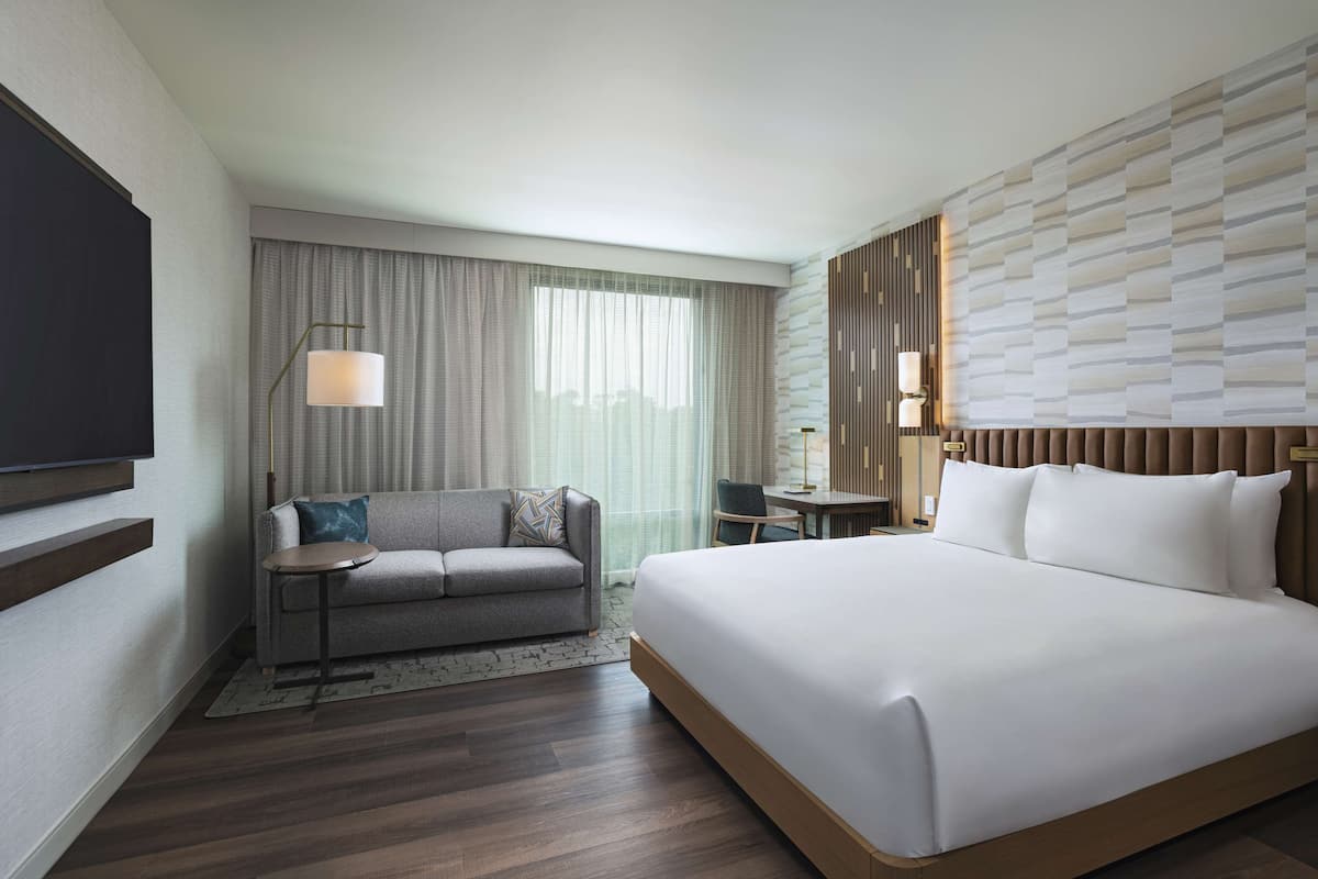 A modern hotel room with a large bed, a sofa, a desk, and a television.