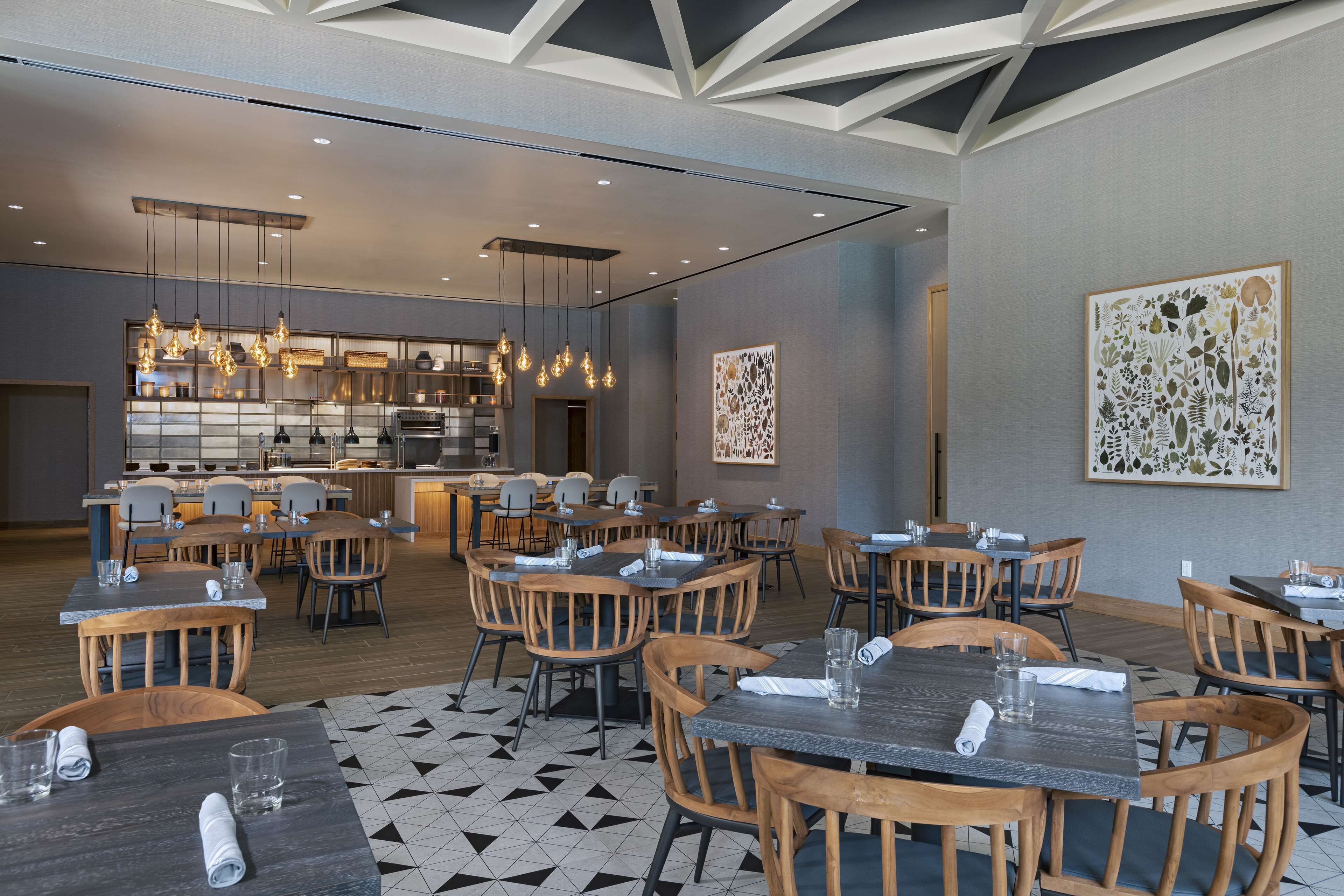 A modern restaurant with wooden tables and chairs, a kitchen area, and decorative wall art.
