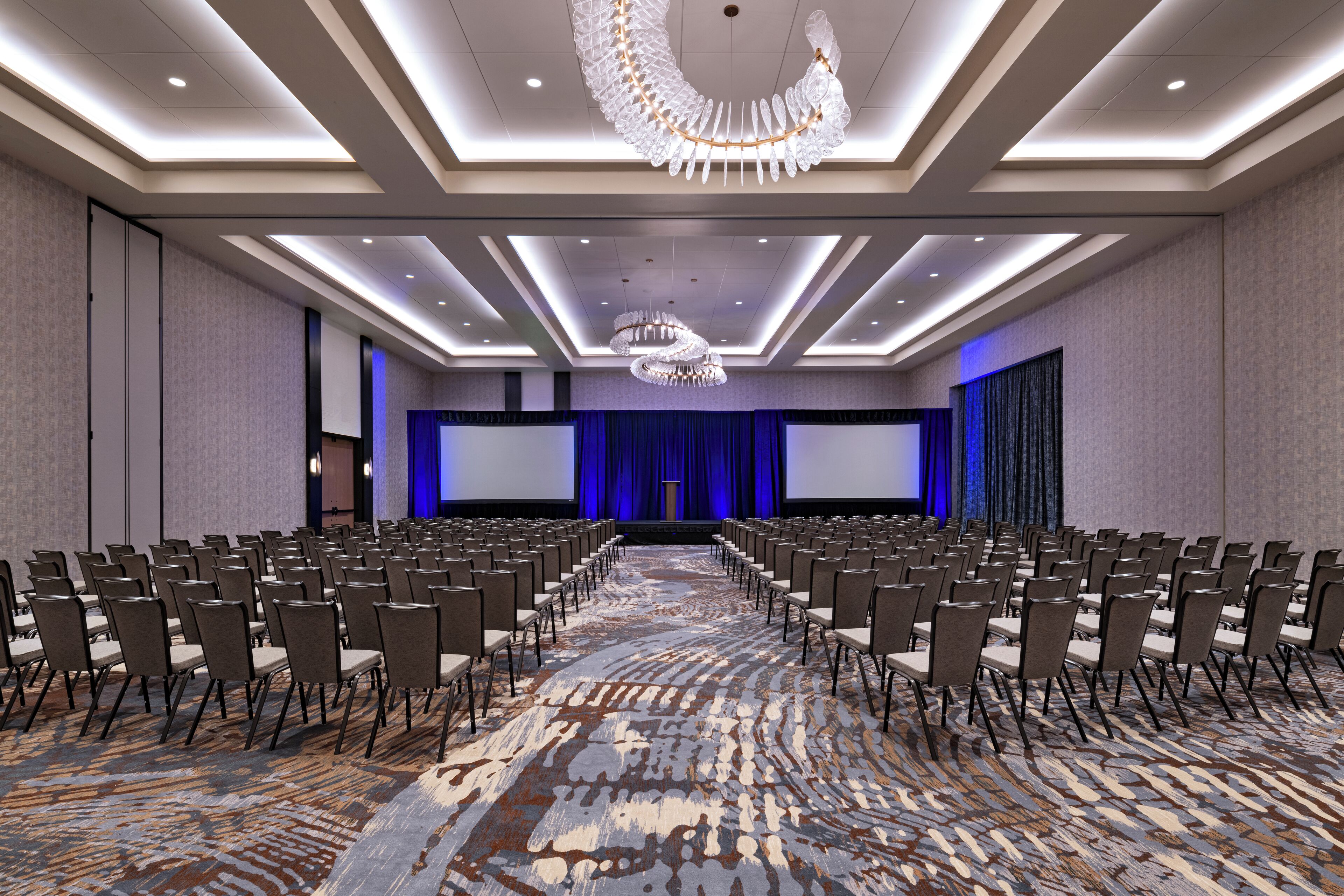 A conference room with rows of chairs, a large screen, and a stage with curtains.