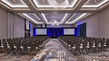 A conference room with rows of chairs, a large screen, and a stage with curtains.
