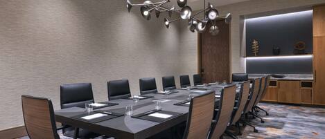 A conference room with a long table, multiple chairs, a modern chandelier, and a wooden cabinet with decorative items.