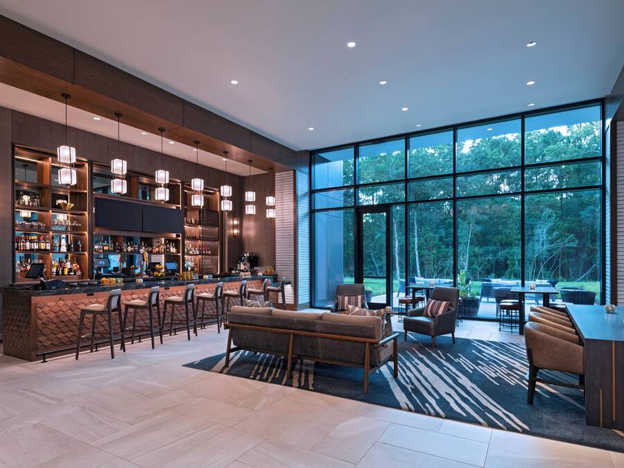 A modern bar area with a long counter, bar stools, and a seating area with sofas and chairs.