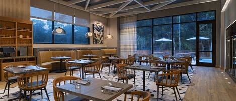Un restaurant moderne doté d’un plafond au design géométrique, de grandes fenêtres et d’un mobilier combinant bois et métal.