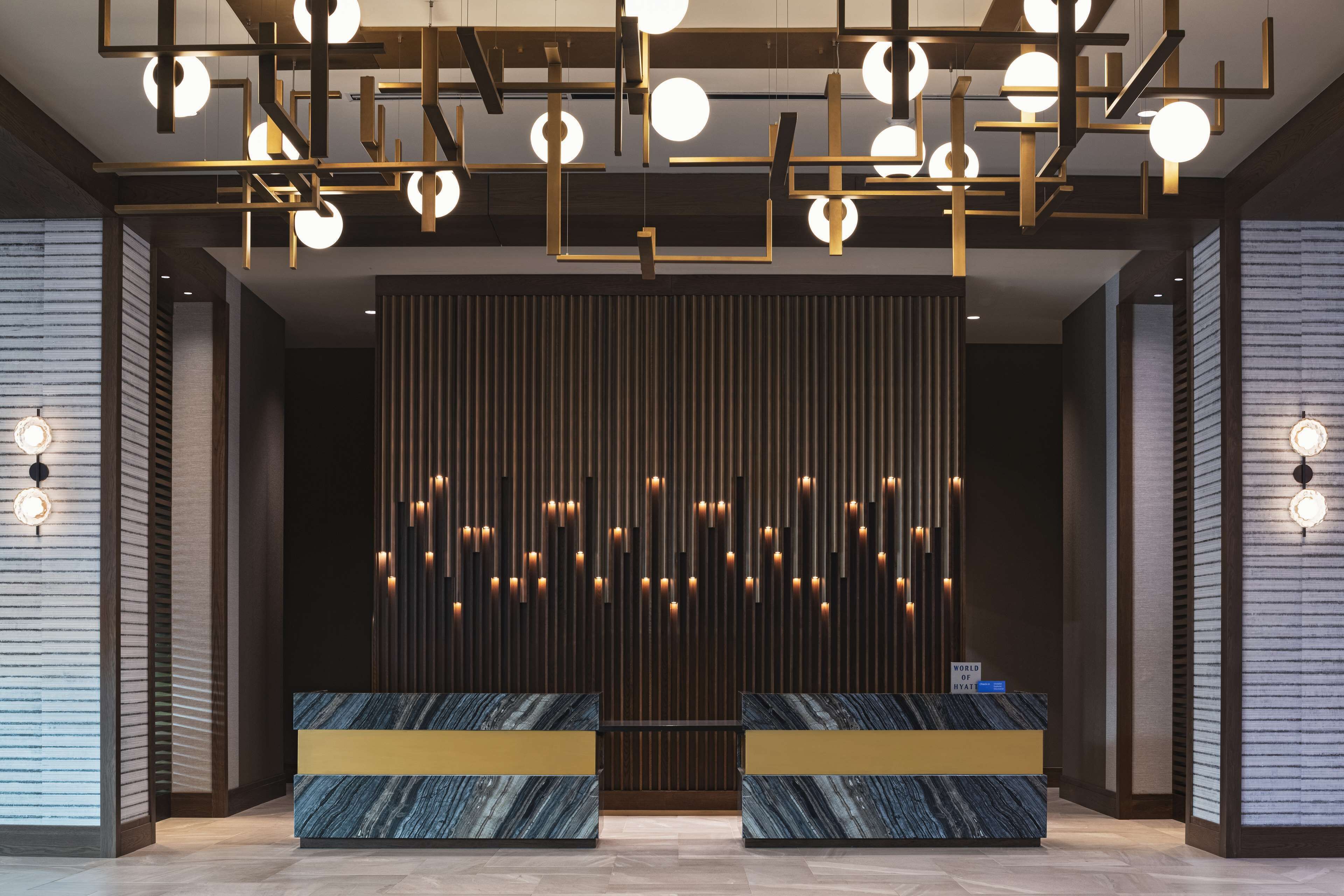 A modern reception area with a dark wood panel wall, a reception desk, and a ceiling with geometric light fixtures.